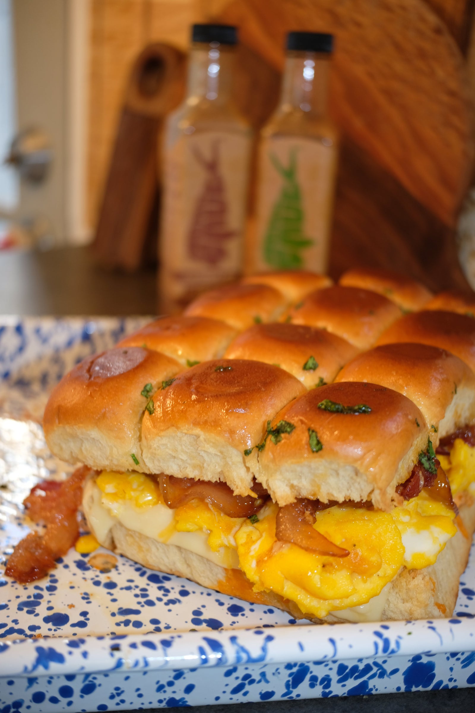 Sweet and spicy pull-apart breakfast sliders with eggs, cheese and Honey Habanero candied bacon on Hawaiian rolls, with Hank Sauce bottles behind